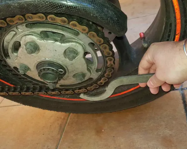Mano con chiave inglese che lavora sulla catena di una moto, mostrando come tirare la catena della moto per la manutenzione.