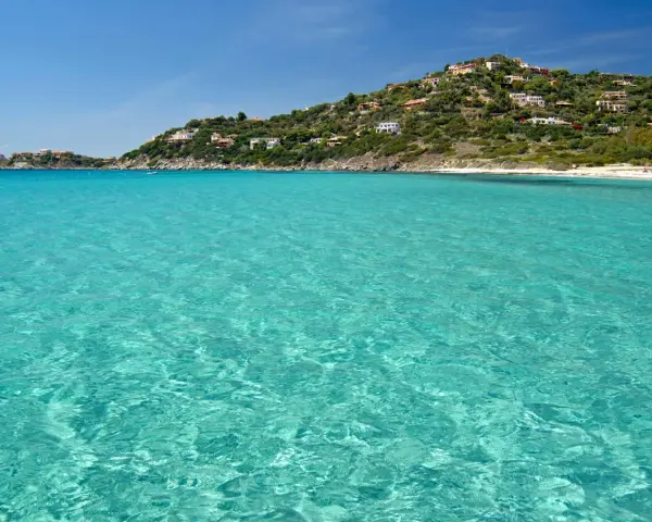 Acque cristalline e una collina verdeggiante punteggiata di case bianche e rosse, con la **spiaggia Torre delle Stelle** che si estende in lontananza.