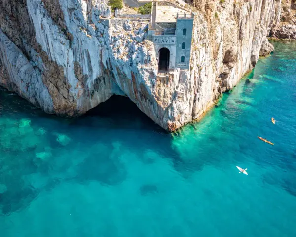 Porto Flavia, un'antica struttura legata alle miniere abbandonate della Sardegna, si affaccia su un mare cristallino. Kayak solcano le acque turchesi.
