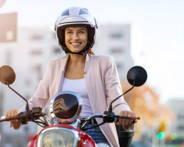 Donna sorridente in motorino, con casco bianco, rispetta l'obbligo casco motorino per la sua sicurezza.