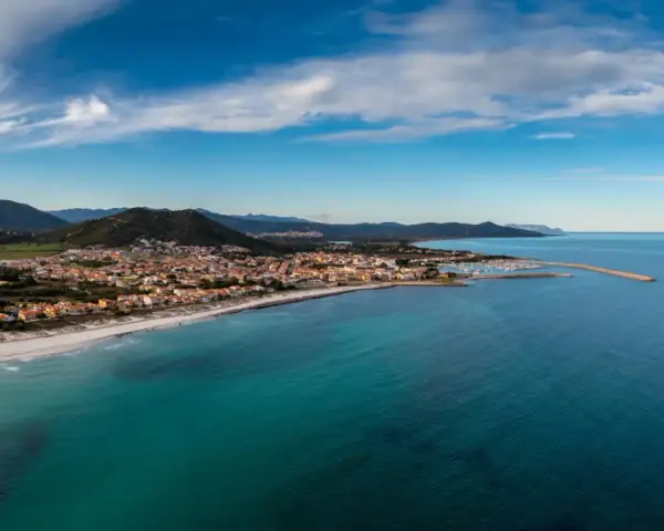 Vista aerea di Posada, Siniscola, con la sua spiaggia dorata, il mare turchese e le case colorate che si affacciano sulla costa.