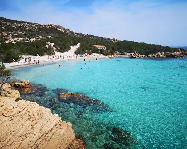 La **cala Granara** splende con acque cristalline e una spiaggia affollata di bagnanti. Rocce dorate emergono dal mare turchese.