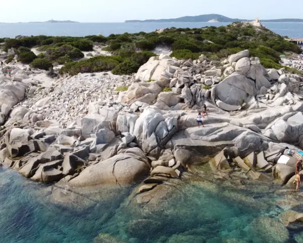 Scogliere rocciose e acque cristalline sulle spiagge a Villasimius. Turisti esplorano la costa selvaggia e si godono il sole.