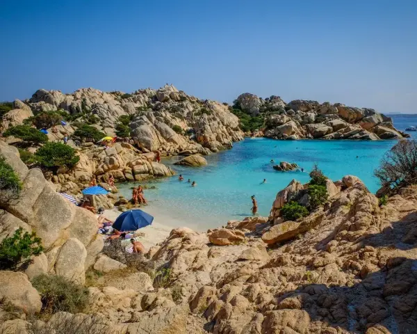 Una baia con rocce granitiche scolpite dal vento e acque turchesi cristalline, tra le spiagge più belle sardegna nord. Gente rilassata sotto gli ombrelloni.