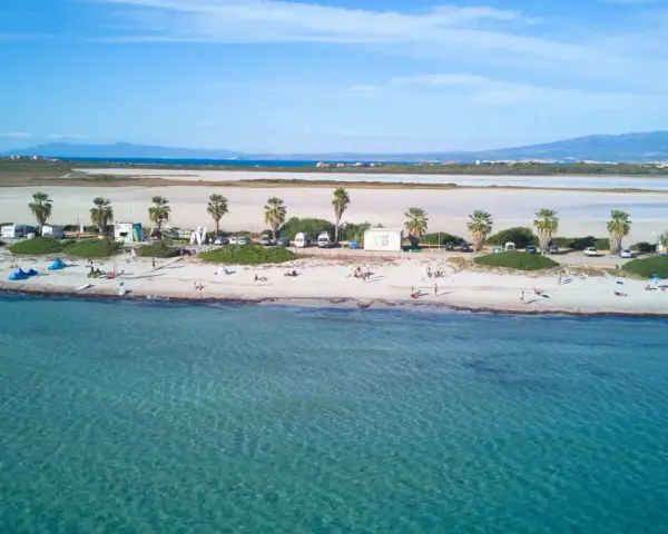 Spiaggia di Putzu Idu con palme, camper e gente che si gode il sole. Acqua cristallina e cielo azzurro.