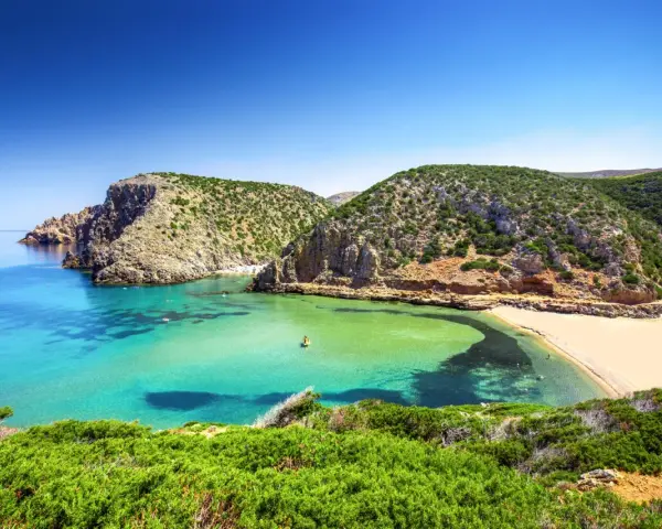 Baia con acque cristalline e sabbia dorata, incastonata tra scogliere verdi. Un vero gioiello tra le spiagge più belle in Sardegna.