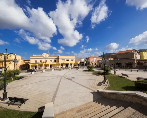 Piazza di San Giovanni Suergiu con edifici gialli e cielo azzurro.