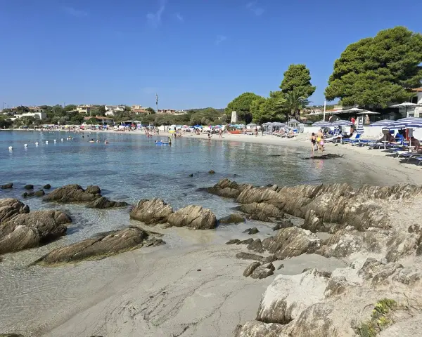 Spiaggia del Pellicano: sabbia chiara, rocce levigate e mare cristallino con bagnanti e ombrelloni.