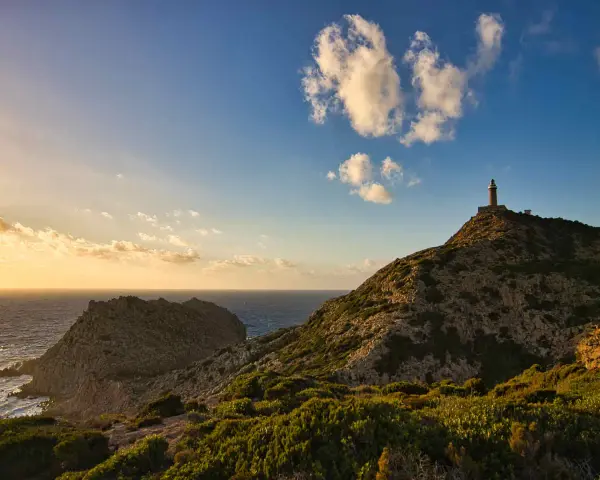 Faro solitario su una collina rocciosa, con il mare e le nuvole al tramonto. Un paesaggio mozzafiato di Nebida, Sardegna.