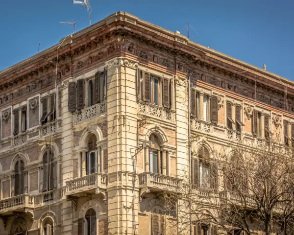 Angolo del **Palazzo Accardo a Cagliari**, con facciata in pietra chiara, balconi in ferro battuto e finestre con persiane.