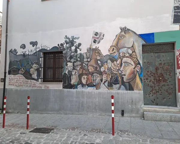 Un grande murale colorato decora un edificio in un paese, con volti, un cavallo e bandiere. Un'opera d'arte che racconta storie di un paese, murales in Sardegna.