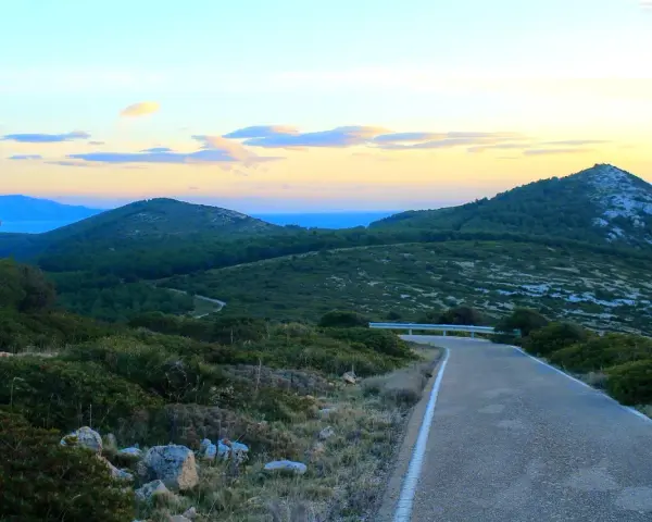 Strada panoramica verso il monte Doglia al tramonto, con colline verdi e cielo colorato.