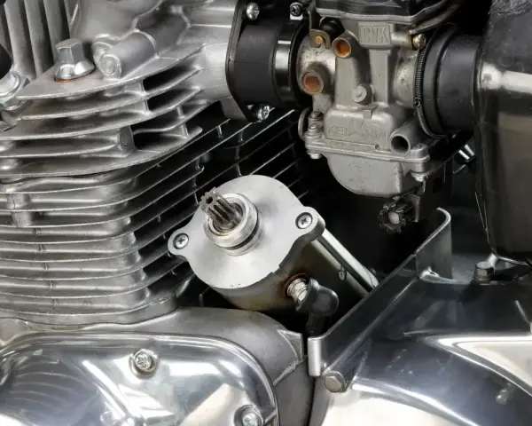 Dettaglio del motore di una moto: il test del motorino di avviamento è in primo piano, con il carburatore e le alette di raffreddamento visibili.
