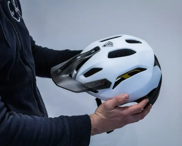 Mani che tengono la calotta esterna di un casco da bici bianco con visiera scura e logo Dainese.