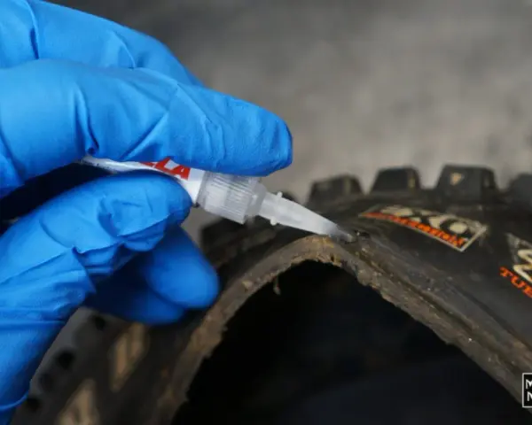 Mano con guanto blu applica colla per pneumatici tubeless riparazione su un copertone da MTB.