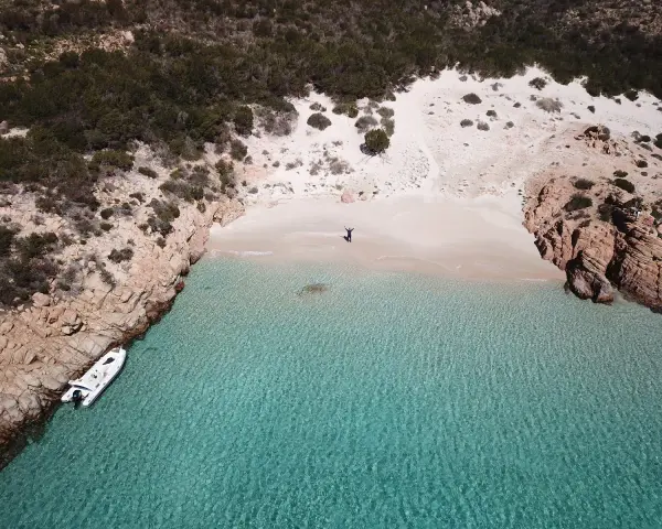 Una persona celebra la bellezza di Cala Soraya, con acque cristalline e rocce rosse. Una barca è ormeggiata.
