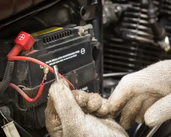 Mani guantate lavorano sulla batteria 12V della moto, forse per il tempo di ricarica.