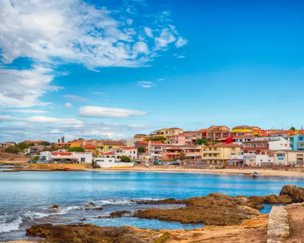 Colorate case affacciate sul mare blu, con rocce in primo piano. Il centro storico di Porto Torres, un incanto sardo.
