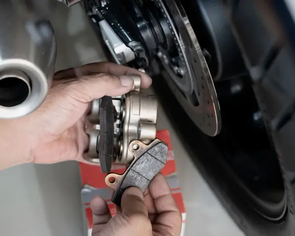 Mani che sostituiscono pastiglie cristallizzate su una moto. Si vede la pinza del freno e il disco.