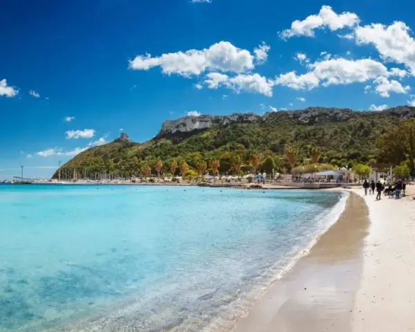 Spiaggia con acque cristalline e la sagoma della Sella del Diavolo all'orizzonte, sotto un cielo azzurro con nuvole bianche.