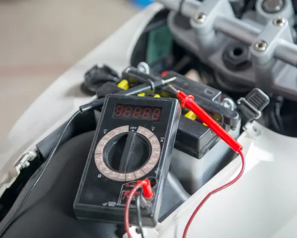 Multimetro collegato alla batteria della moto per verificarne lo stato prima di staccare la batteria moto inverno.