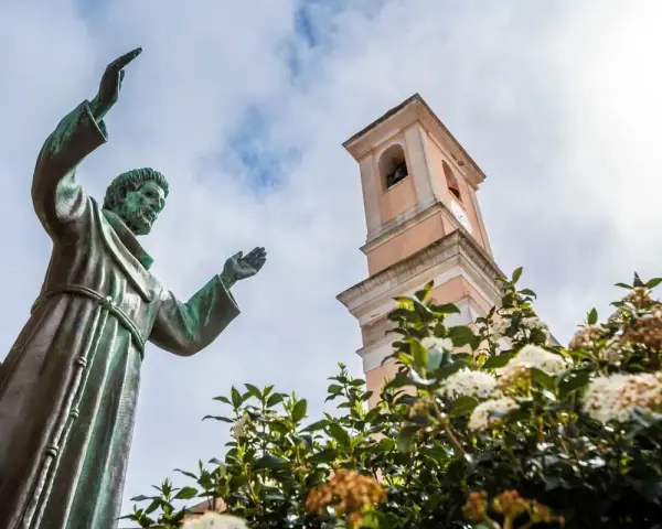 Statua di San Francesco con campanile e fiori. Il **Nuoro significato** di questo luogo è legato alla spiritualità e alla natura.