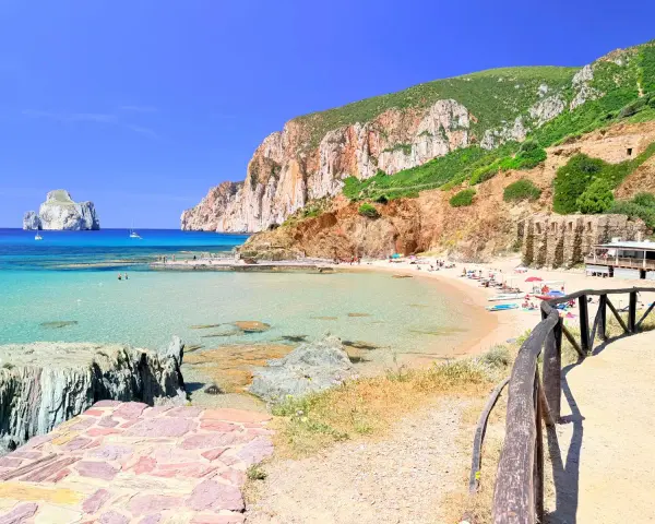 Spiaggia di Masua con acque cristalline, scogliere imponenti e il Pan di Zucchero all'orizzonte. Relax e natura incontaminata.