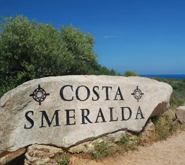 Masso con scritta "COSTA SMERALDA" in Sardegna, dove il mare azzurro incontra la macchia mediterranea.