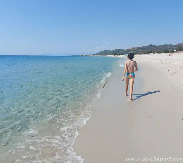 Bambino cammina su una delle splendide spiagge della costa est della Sardegna, con mare cristallino e sabbia bianca.