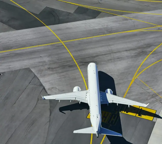 Aereo bianco in attesa sulla pista di uno degli aeroporti della Sardegna, con segnaletica gialla che guida il traffico aereo.