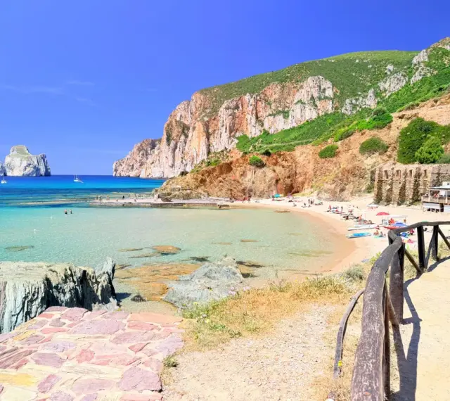 Spiaggia di Masua con acque cristalline, scogliere imponenti e il Pan di Zucchero all'orizzonte. Relax e natura incontaminata.