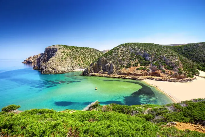 Baia con acque cristalline e sabbia dorata, incastonata tra scogliere verdi. Un vero gioiello tra le spiagge più belle in Sardegna.