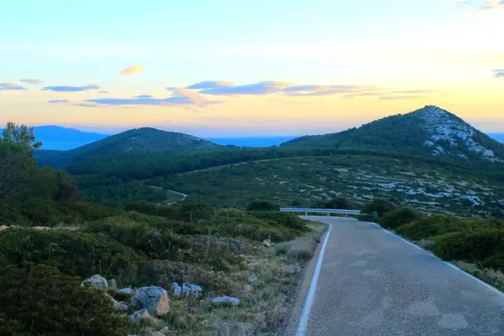 Strada panoramica verso il monte Doglia al tramonto, con colline verdi e cielo colorato.