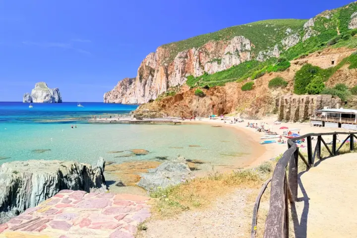 Spiaggia di Masua con acque cristalline, scogliere imponenti e il Pan di Zucchero all'orizzonte. Relax e natura incontaminata.