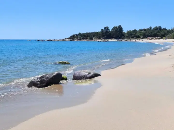 Spiaggia di Lido di Orrì con rocce scure bagnate dall'acqua cristallina e sabbia dorata.