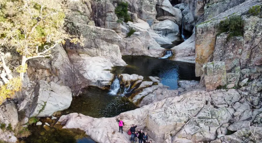 Un gruppo di escursionisti ammira un canyon con cascate e pozze d'acqua cristallina. Uno di loro, con un giubbotto rosa acceso, sembra dire "bau mela!" alla natura.