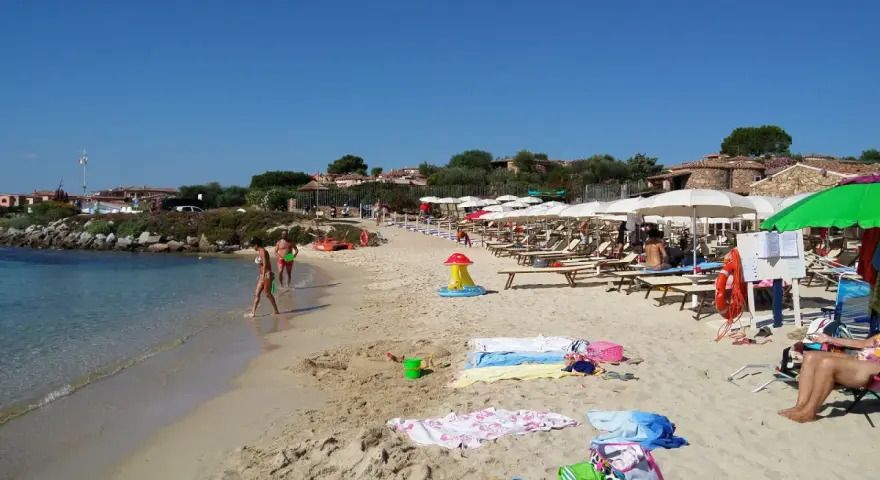 A sunny beach with people walking in the shallow water and lounging under umbrellas.