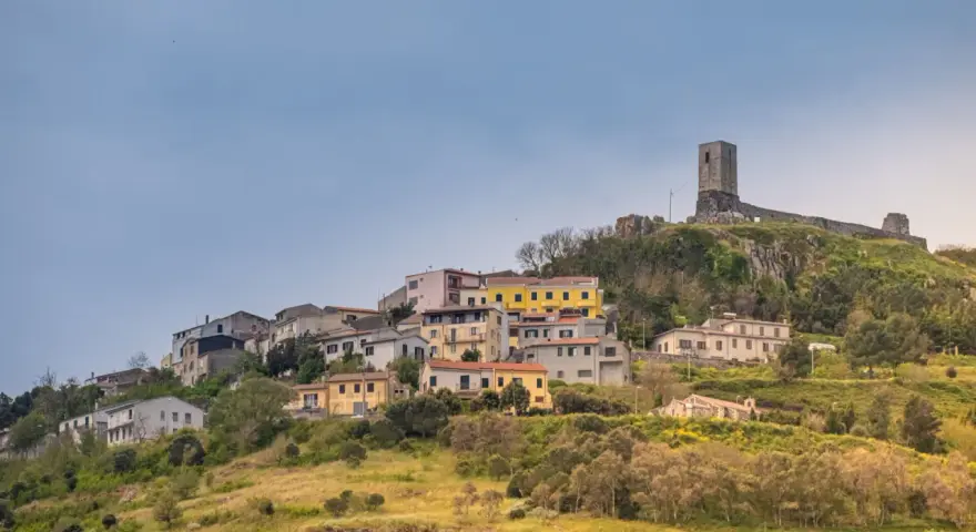 Il castello di Osilo domina un borgo colorato su una collina verdeggiante, sotto un cielo azzurro.