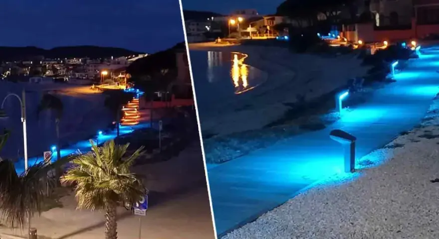 Passeggiata illuminata da luci blu sul lungomare di Golfo Aranci sera, con palme e case sullo sfondo.