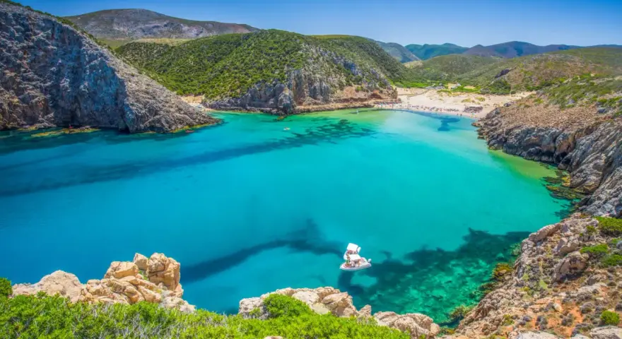La splendida spiaggia di Buggerru, con acque cristalline e rocce imponenti, invita al relax. Una barca bianca solca il mare turchese.