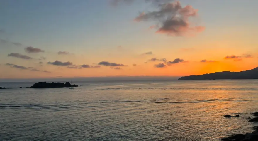 Un tramonto mozzafiato sul mare, con un'isola rocciosa e una barca a vela. Un luogo perfetto per ammirare dove vedere il tramonto a Villasimius.