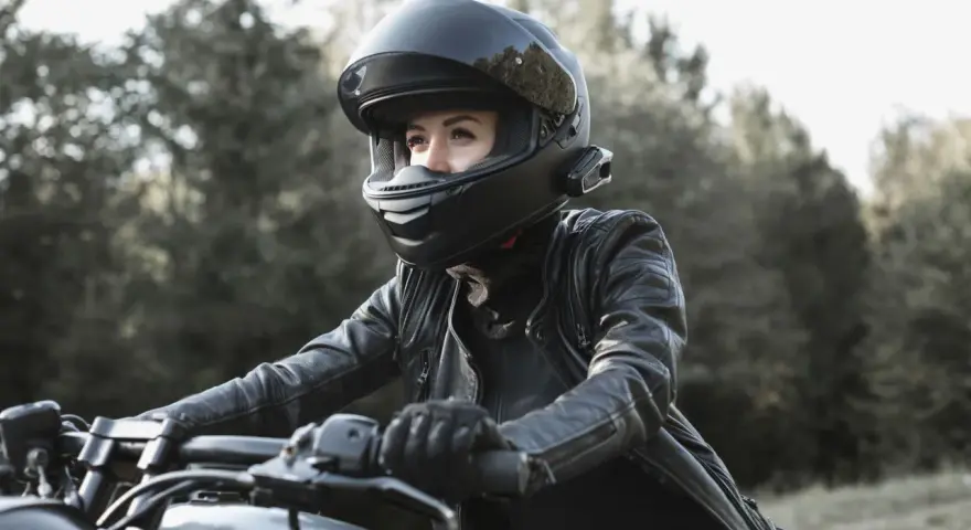 Woman in black leather jacket and helmet riding a motorcycle outdoors.