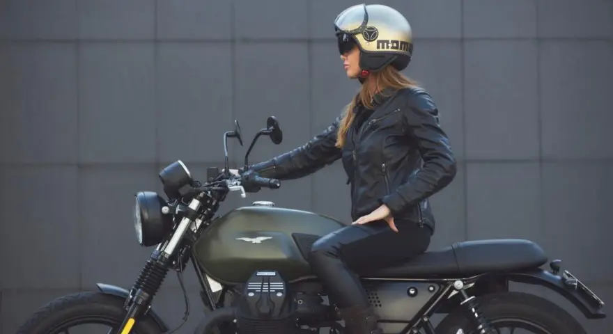 Donna in giacca di pelle e casco dorato, seduta su una moto verde. Non è chiaro dove si buttano i caschi da moto, ma questo è un ottimo esempio di come indossarli.