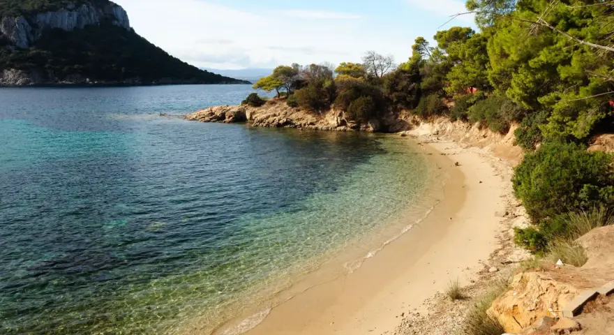 Spiaggia dorata e acque cristalline nella baia di Cala Moresca, con una scogliera verdeggiante e un promontorio roccioso sullo sfondo.