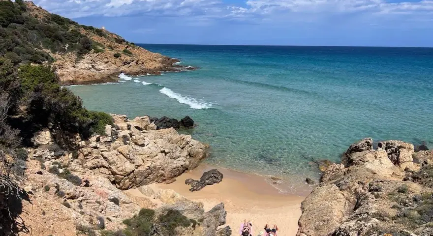 Spiaggia selvaggia vicino al centro storico di Chia, con rocce dorate, mare cristallino e due persone che prendono il sole.