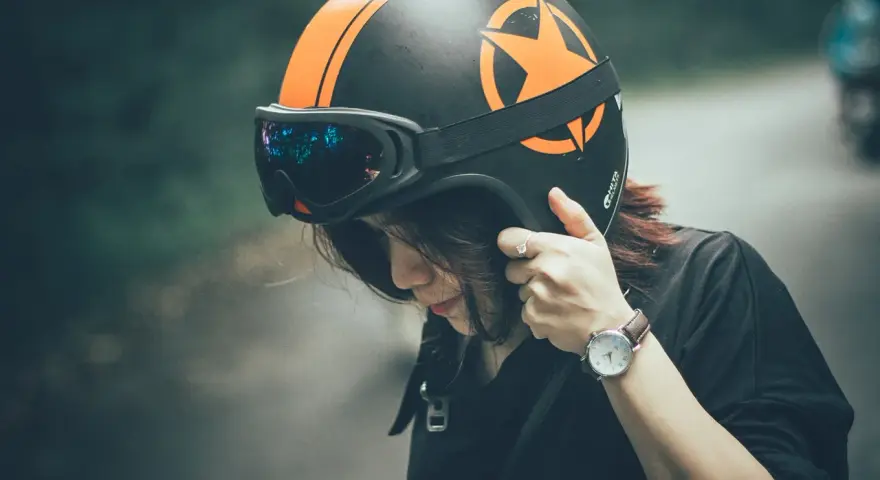 Ragazza con casco moto nero e arancione, occhiali vintage. Guida sicura: come scegliere casco moto.