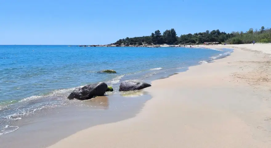 Spiaggia di Lido di Orrì con rocce scure bagnate dall'acqua cristallina e sabbia dorata.