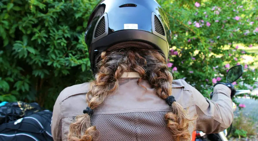 Donna con casco nero e capelli raccolti in due trecce, pronta per legare il casco alla moto.
