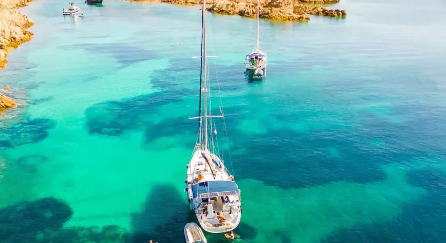 Vela al largo di Cala Ambra, con acque cristalline e un paesaggio roccioso.