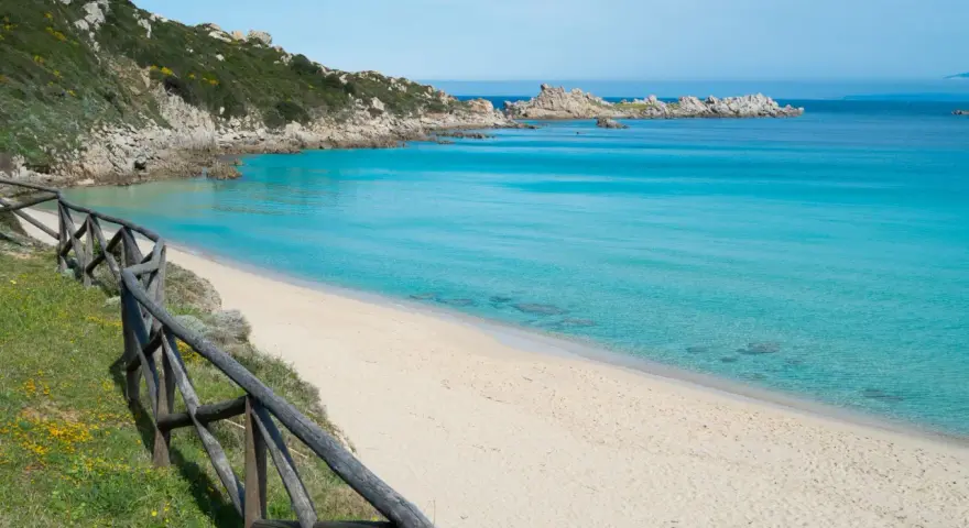 Una splendida spiaggia rena bianca bagnata da un mare cristallino. La vegetazione mediterranea e le rocce scolpite dal vento completano il paesaggio.